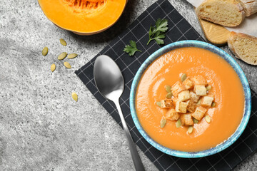 Tasty creamy pumpkin soup served with bread on grey table, flat lay. Space for text