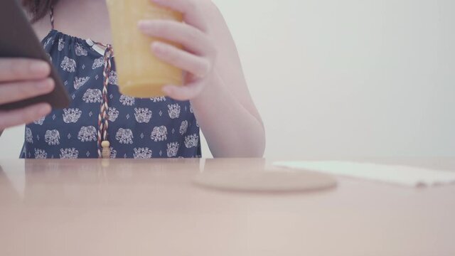 Slow motion Asian tourist woman chatting smartphone and dink orange juice in vintage cafe. Relaxing lifestyle travel in coffee shop after quarantine coronavirus with new normal social distancing