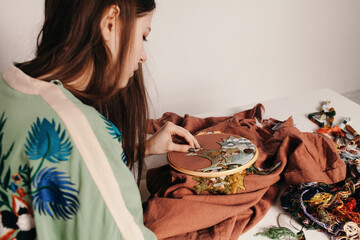 Focused woman working with embroidery at messy table