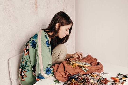 Focused woman working with embroidery at messy table