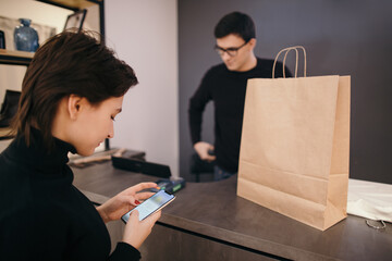 Female client with mobile phone preparing for payment in shop