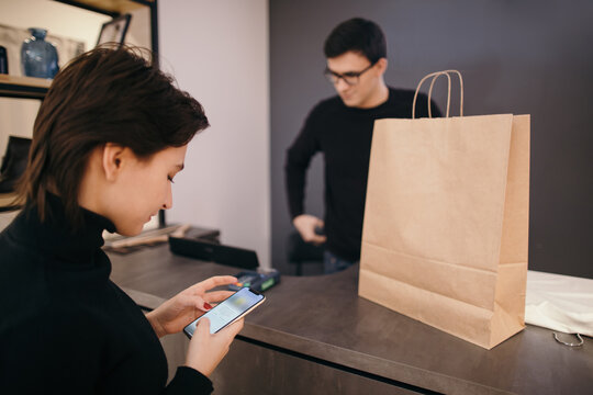 Female client with mobile phone preparing for payment in shop