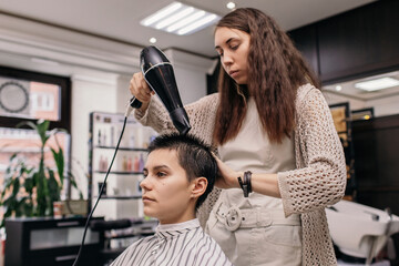 Hairstylist drying hair of cheerful androgynous customer