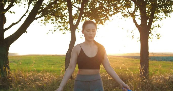 Portrait of young Asian female athlete exercising on road outdoor sunrise and jumping with jump rope. Joyful beautiful sporty woman working out. Training concept. Healthy lifestyle