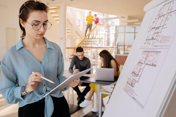 Smart architect with tablet standing near whiteboard with drafts