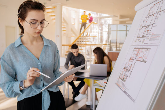Smart architect with tablet standing near whiteboard with drafts