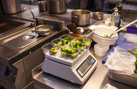 Plastic boxes with vegetables on scale in kitchen