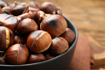 Delicious roasted edible chestnuts in bowl on table, closeup