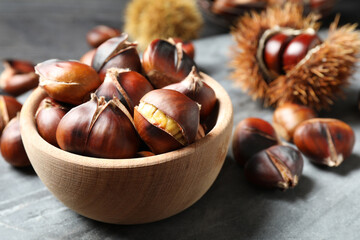 Delicious roasted edible chestnuts in wooden bowl on grey marble board, closeup