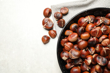 Obraz premium Delicious roasted edible chestnuts on light grey table, flat lay. Space for text