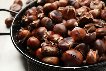 Delicious roasted edible chestnuts in frying pan on table, closeup