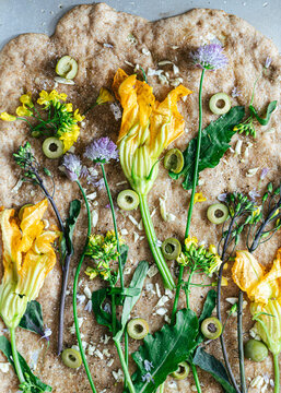 Baked flatbread with zucchini flowers, kale flowers, olives and chives