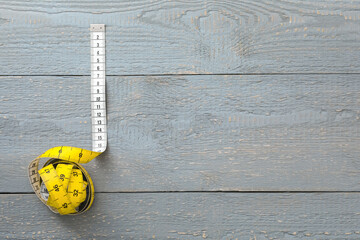 Yellow measuring tape on light grey wooden table, top view. Space for text