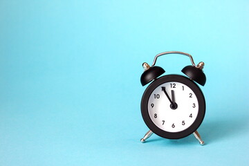 The clock is 23-55. Black alarm clock on a blue background. The concept of the New year and...