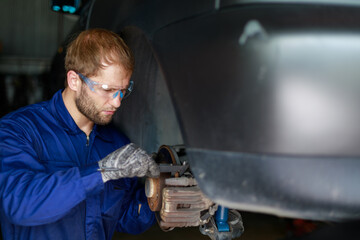 A male auto mechanic in uniform is examining a brake while working in auto service