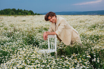 Tall handsome man standing near white chair in camomile flowers field