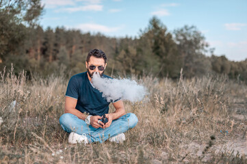 Stylish brutal vape man exhaling vapor from electronic cigarette in the fresh air. Modern ways of...