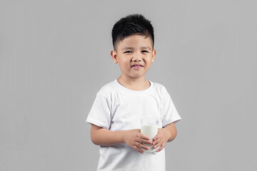 Asian child drinking milk from a glass on gray background