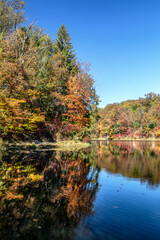 Colorful fall foliage is reflected upon the surface of beautiful Strahl Lake under a deep blue sky, located in Brown County State Park, Indiana.