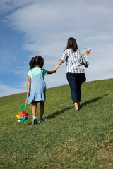 Fototapeta premium Mother and daughter holding turbine toy and holding hand together going up to the top of the hill to enjoy with beautiful nature.