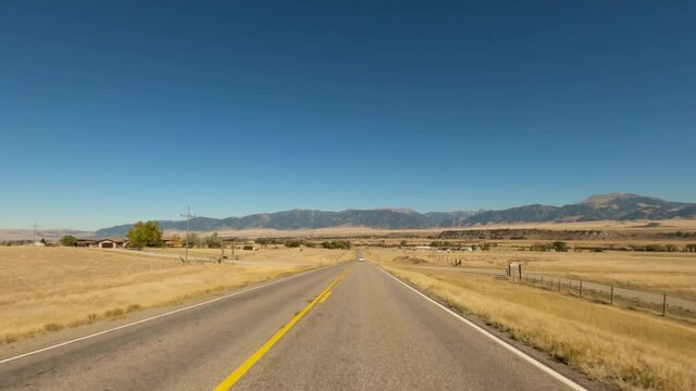 Long straight Highway 287 toward Ennis Montana passing dry amber fields with the Madison range in the background-Drive Plate-POV