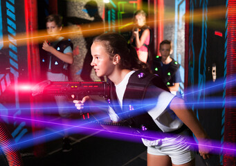 Portrait of teenager girl with laser gun having fun on dark lasertag arena..