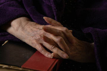 Elderly person clasps hands on top of a red and black covered book