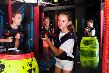 Portrait of teenager girl with laser gun having fun on dark lasertag arena..