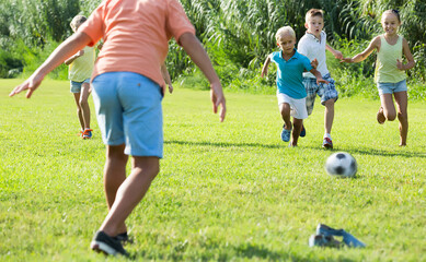 Obraz na płótnie Canvas Group of happy kids in school age happily playing football together on green lawn in park