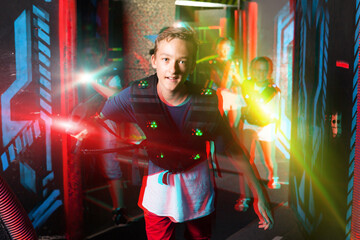Portrait of teenager boy with laser gun having fun on dark lasertag arena..