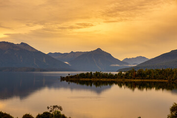 Beautiful Lake Te Anau scenery and water reflections under a vibrant  orange coloured sky at sunset