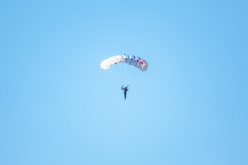 one parachutist floats slowly at low altitude on the background of clear sky