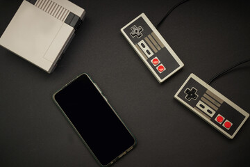 retro console and controls and cell phone on black background