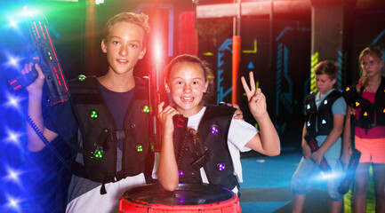 Portrait of excited teen boy and girl with laser guns during lasertag game in dark room..