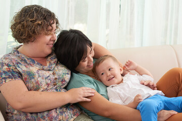 Smiling woman with her wife and little son resting at home on weekend