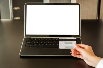 Obraz na płótnie Canvas Online payments. Banking transfer. Digital technology. Female hand holding credit card near laptop blank screen in workplace interior copy space.