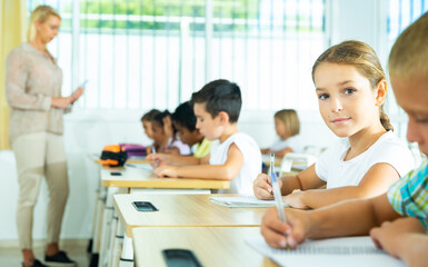 Fototapeta premium Portrait of cheerful preteen girl elementary school student looking at camera during lesson