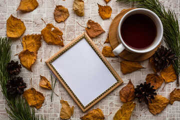 Naklejka na ściany i meble Empty photo frame and black tea cup against pastel shades background with autumn leaves among pine branches and cones. Memories of past concept. Copy space. Top view