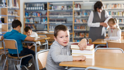 Portrait of smiling preteen boy sitting with pile of textbooks in school library