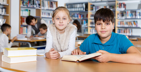 Cute tween girl and intelligent boy studying together in school library, reading books