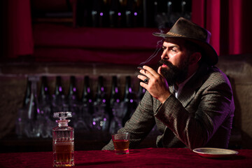 Handsome bearded man enjoying whiskey in bar. Hipster with beard drinking a brandy in bar. Brutal guy drinking alcohol.