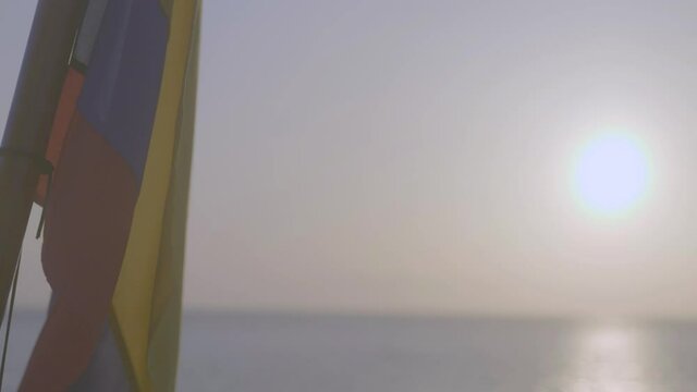 The sun can be seen while a flag of Ecuador or Colombia is flaming and moving because of the wind. The flag is yellow, blue and red.