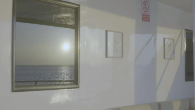 On the window of a wall the sun and the ocean are being reflected. Some paintings are hanging on the wall as well.