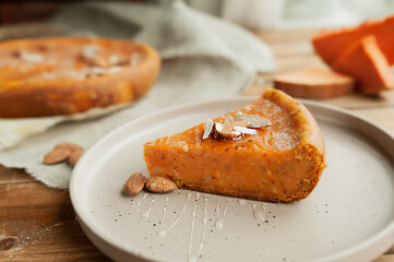 piece of pumpkin pie with almonds and honey, whole pie on rough canvas napkin on wooden table with pieces of pumpkin, honey, cozy home-made autumn dinner, selective focus