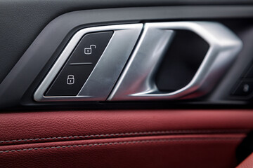 Fototapeta na wymiar Сlose up of a door control panel with chrome handle on the car door, common black and red genuine leather in a new car. Arm rest with control buttons