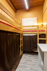 Wooden bunk beds with curtains in a large hostel dorm room