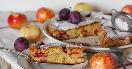Laid table with a sweet round pie with apples and plums. Homemade biscuit charlotte with powdered...