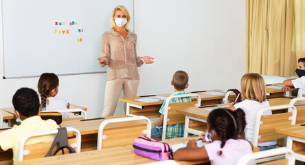 Portrait of woman teacher in protective face mask explaining new theme during class, new normal...