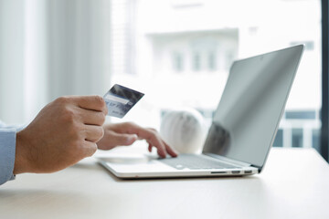 The businessman's hand is holding a credit card and using a laptop for online shopping and internet payment in the office