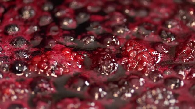 The raspberry and blueberry sauce is bubbling in the pot. Close up. Pan motion shot.